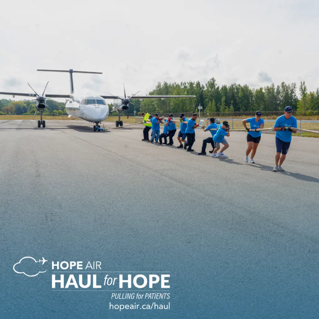 a number of people wearing hope air t-shirts pulling a thick rope connected to a small plane behind them