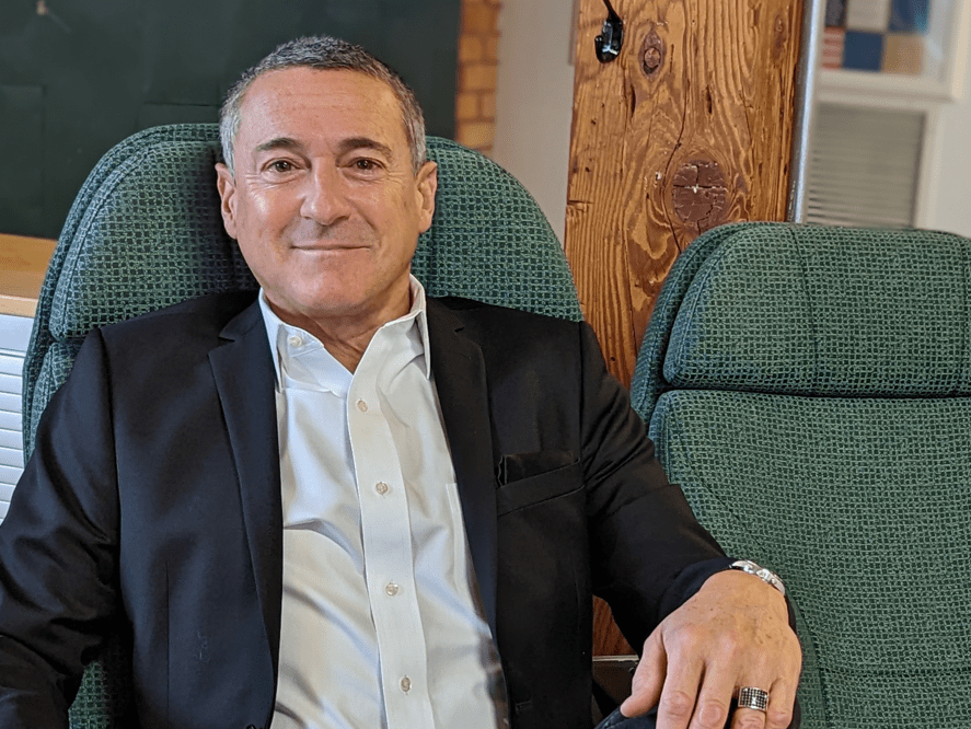 a man smiling casually wearing a blazer and sitting in a green fabric chair