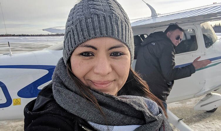Une femme portant une toque sourit devant un pilote et un avion.