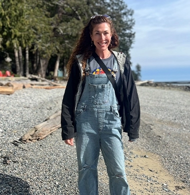 A woman smiling at the camera as she walks along a pebble beach
