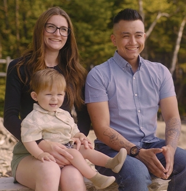 Two parents smiling holding their young son while sitting outside on a bench