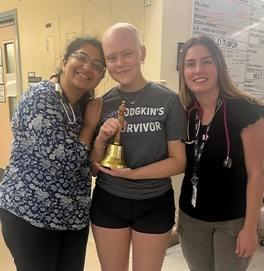 A woman holding a bell symbolizing her cancer survivor journey in a hospital hallway