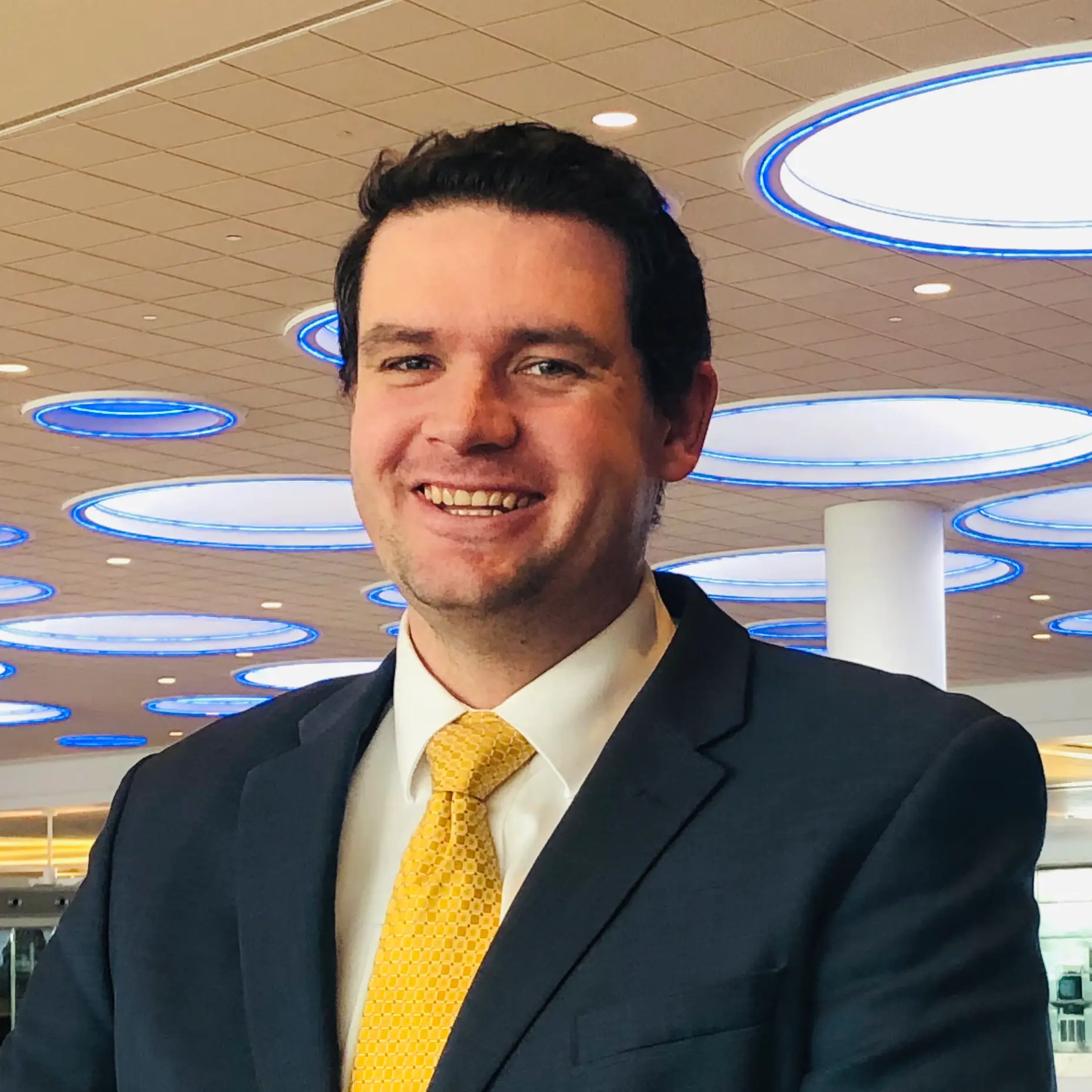 A headshot of James Lindsey smiling and wearing a blazer and yellow tie.