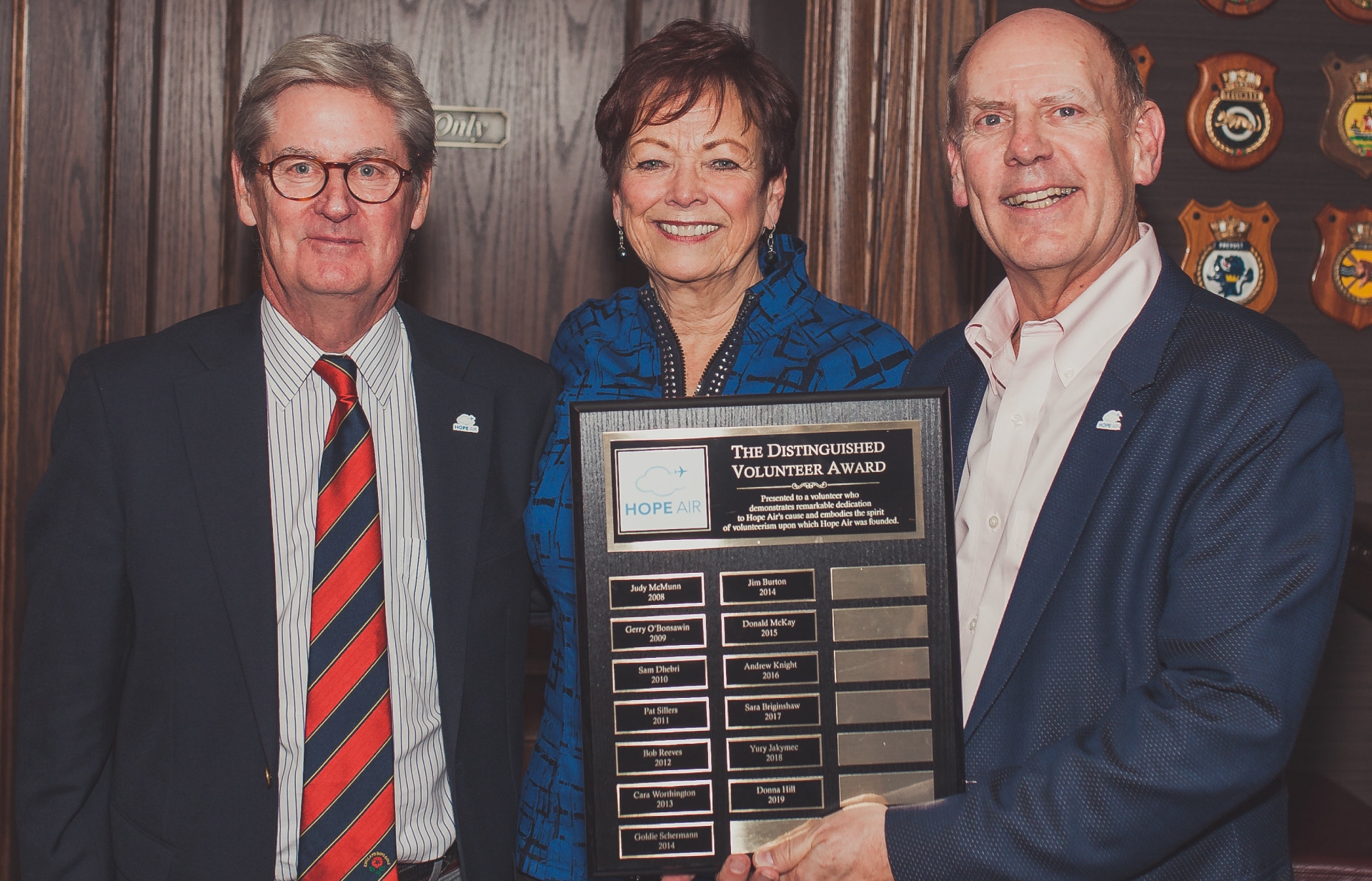 3 people celebrating Hope Air volunteers. They're dressed formally, smiling and holding The Distinguised Volunteer Award