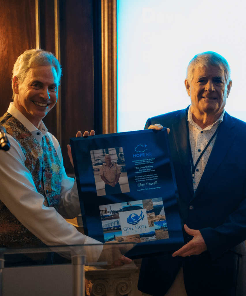 Two men smiling and holding a Hope Air award presented to Glen Powell