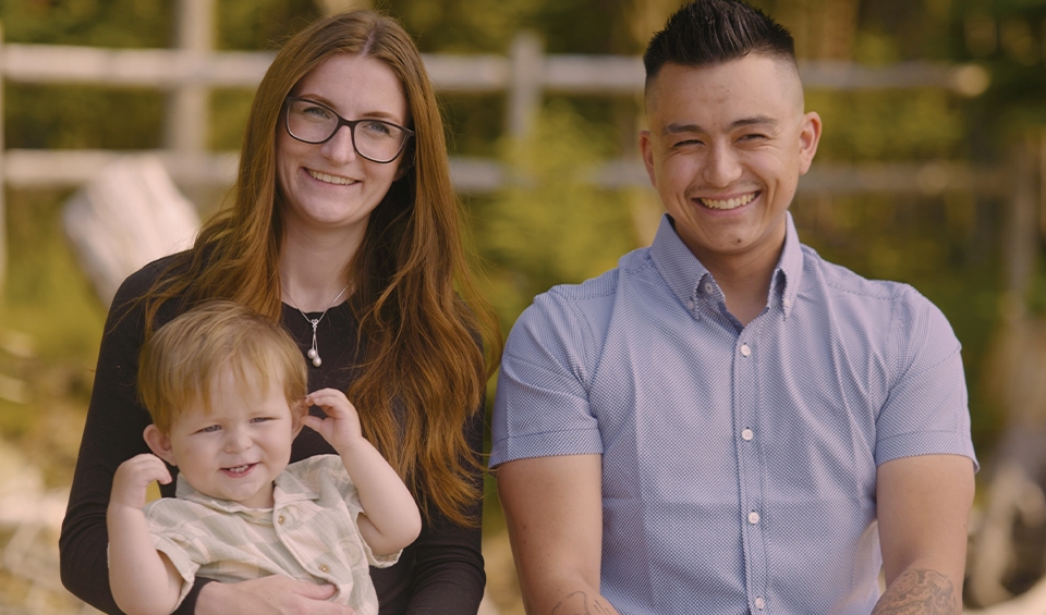 Two parents smiling while holding their young son.