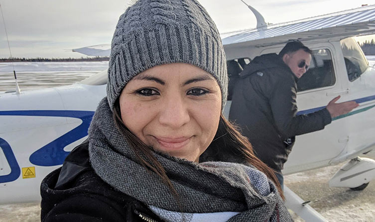 A woman wearing a toque smiles in front of a pilot and an plane