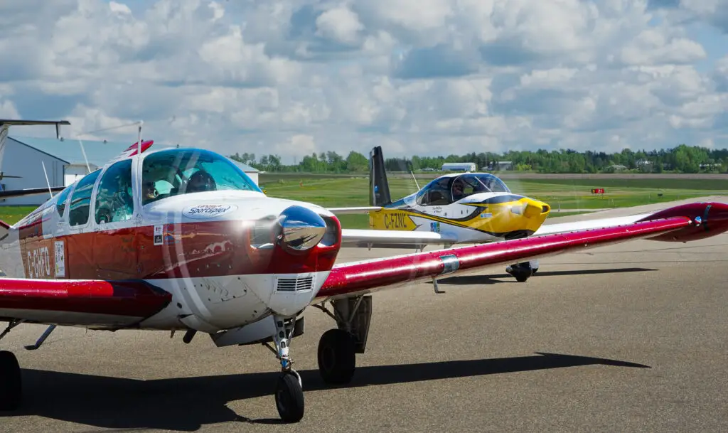 2 small planes in Regina on June 26th, as part of a campaign to raise awareness for charity's medical travel support programs. One is red and one is yellow. The sky is perfectly clear.