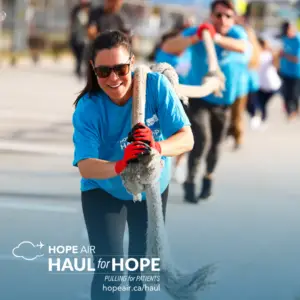 a woman wearing sunglasses and smiling, wearing a hope air t-shirt and participating in a tug-of-war competition