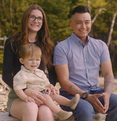 Deux parents souriants, assis sur un banc à l'extérieur, tenant leur jeune fils dans leurs bras