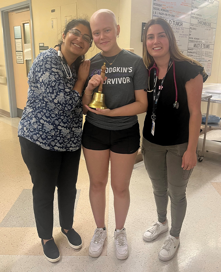 A woman holding a bell symbolizing her cancer survivor journey in a hospital hallway