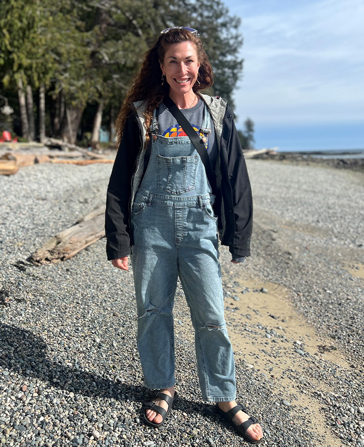 A woman smiling at the camera as she walks along a pebble beach