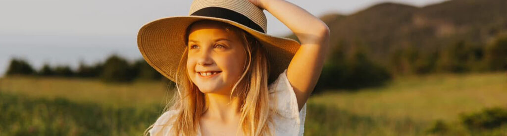 A girl with a sunhat on smiling in a field